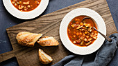 Minestrone soup served with pieces of crusty bread on a wooden serving board