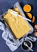 Orange poppy seed cake batter in tin with oranges and a bowl of poppy seeds