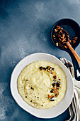 Cheesy mashed potatoes with roasted walnuts and black pepper in a white ceramic bowl