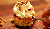 A cupcake with brittle and a cream topping being cut with a fork