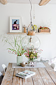 Autumn arrangements with rose hips and book on wooden table below pendant lamp with glass lampshade in rustic dining room