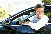 A young business man sitting in a car with the door open