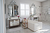 White, rectangular bathtub between twin washstands with opulent mirrors in elegant, luxurious bathroom