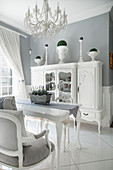 Antik Geschirrschrank in Weiß und Esstisch unter Kronleuchter in elegantem Esszimmer
