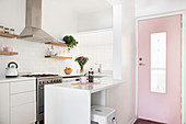 weiße Einbauküche mit Frühstückstheke neben rosa Eingangstür