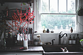 Branches with red berries in white ceramic vase on kitchen counter next to sink