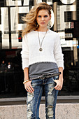 A young blonde woman wearing a t-shirt, a white jumper and jeans