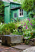 Stone trough as a pond in the garden with a weathered green wooden hut