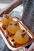 A woman holding a copper tray of apple cider, with cinnamon sticks, star anise, and gold straws