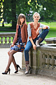 Two women wearing autumnal outfits in shades of brown and blue: a dress with a jacket, and a top with jeans and a cardigan