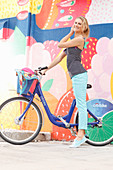 A blonde woman wearing a black-and-white polka dot top and light blue trousers with a bike