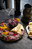 A purple dip with flatbread, oranges and vegetables