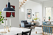 View across dining table to armchair and drinks trolley below staircase in open-plan interior