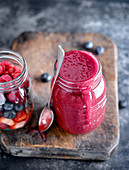 Close-up of glass jar filled up to maximum with red fruit smoothie and served with spoon on wooden board
