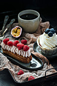 Eclair mit Sahne und Beeren, Vanille-Cupcake und eine Tasse schwarzer Kaffee