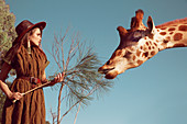 Brünette Frau mit Hut in braunem Kleid und Giraffe