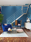 Sitzmöbel und Treppenaufgang in offenem Wohnraum mit blauer Wand