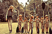 A young woman with children wearing uniforms and holding paddles standing in a field
