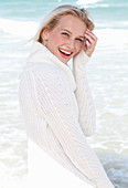 Junge blonde Frau in weißem Pullover am Meer