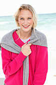 A young blonde woman wearing a pink jumper with a grey jumper over her shoulders