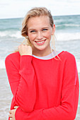 A young blonde woman by the sea wearing a red jumper