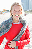 A young blonde woman wearing a red jumper with a grey jumper over her shoulders