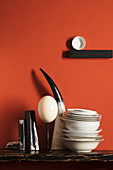 Ostrich egg, cow's horn and porcelain bowls against red wall