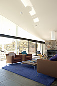 Lounge mit brauner Polstergarnitur, blauem Teppich, Kamin und Glasfront