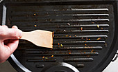 A grill being cleaned with a wooden spatula