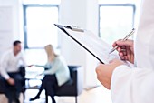 Doctor making notes in foreground with patients in backgroun