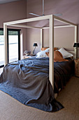 Four-poster bed with dark-blue bedspread in bedroom with brown walls