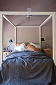 Four-poster bed with dark blue bedspread in bedroom with brown wall