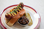 Hot Dog mit Senf und Ketchup, dazu Essiggurke und Zwiebelrelish