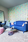 Blaues Sofa vor golden gemusterter Tapete im eleganten Wohnzimmer