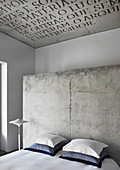 Doppelbett mit Kissen vor Betonwand im Hotelzimmer, Betondecke mit Schrift