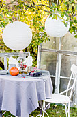 Autumnal arrangement on table below paper lanterns in garden