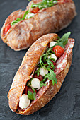 Artisan baguettes on a slate filled with salami, tomatoes, mozzarella balls and rocket