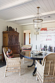 Wicker chairs at round table in dining room with wood-panelled ceiling