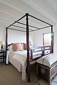 Oriental trunk with large cushion on top at foot of wooden four-poster bed