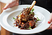 Lamb shank elegantly stacked with coriander seeds and micro herbs