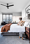 Double bed in the bedroom with gray carpeting, in the background a bench