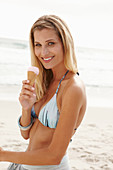 Blonde Frau mit Eis im Bikini am Strand