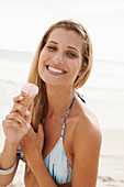 A mature blonde woman on a beach wearing a bikini and holding an ice cream