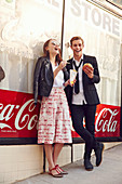 A young couple standing against a wall holding fast food