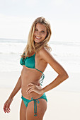 A blonde woman on a beach wearing a turquoise bikini