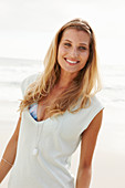 A mature blonde woman on a beach wearing a long top