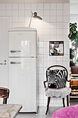 White retro fridge and chair with zebra cushion against white-tiled wall