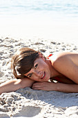 A mature brunette woman on a beach wearing a red bathing suit