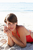 A mature brunette woman on a beach wearing a red bathing suit