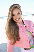 Junge blonde Frau in bedrucktem T-Shirt und rosa Jeansjacke am Strand